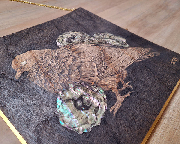 Close up view of a wood panel with an inlayed wood design of a bird and flowers made of abalone flowers.