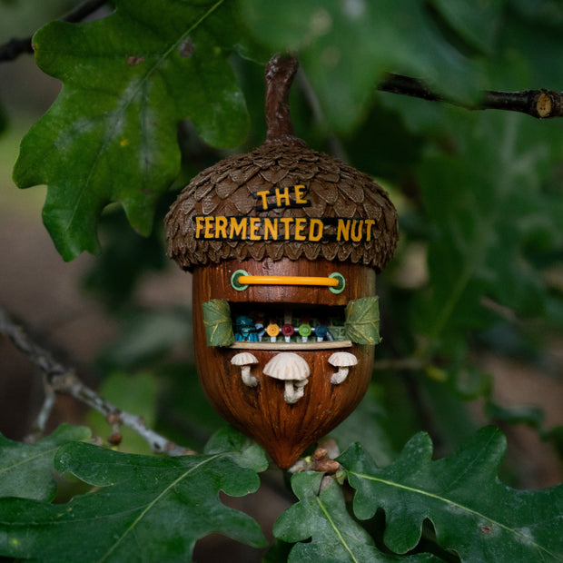 Decorative acorn-shaped sculpture, fashioned into a miniature bar with 'The Fermented Nut' text on its roof and mushroom stools in front of several beer taps.