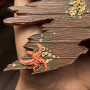Sculpture made of wood of a ripped part of a ship, close up to show many barnacles on the side of the wood and a tiny starfish.