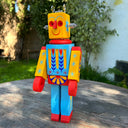 Wooden sculpture of a toy robot, painted in bright yellow, red and blue with floral and starburst patterns. It has a metal coil on its head and lightbulbs coming out the side of its head.