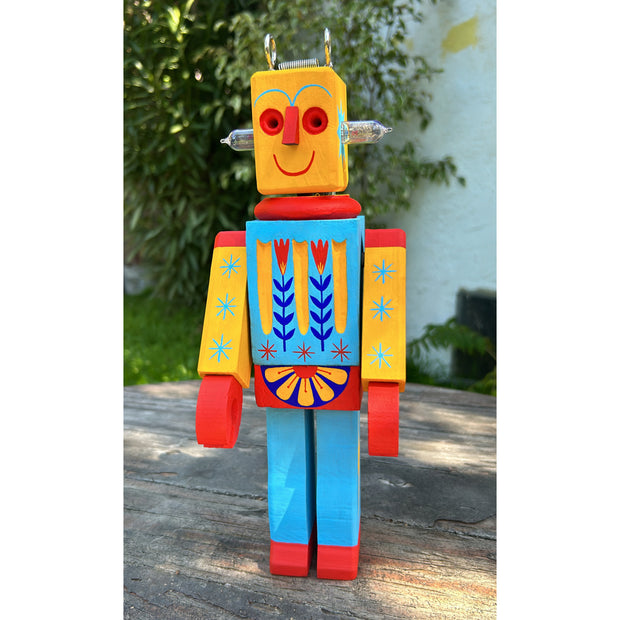 Wooden sculpture of a toy robot, painted in bright yellow, red and blue with floral and starburst patterns. It has a metal coil on its head and lightbulbs coming out the side of its head.