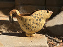 A ceramic horse-shaped pitcher with a cream and brown speckled glaze, resting outdoors on a stone surface.