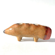 Ceramic sculpture of a brown dog made to look like a pencil, with a pointed tip black nose and a pink eraser shaped butt. It has several holes atop its back to hold pens.
