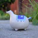 Ceramic sculpture of a very, very chunky white horse with a tiny head, tiny legs and a tiny blue tail. It has a blue blanket over its back.