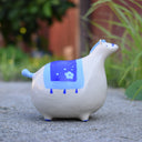 Ceramic sculpture of a very, very chunky white horse with a tiny head, tiny legs and a tiny blue tail. It has a blue blanket over its back.
