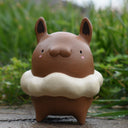 Ceramic figure of a cute, brown animal-like character with a fluffy cream colored fur collar around its neck.