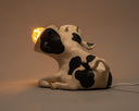 Lamp designed as a cow's body sitting on the ground, with 2 light bulbs coming from 2 separate cow heads conjoined to the same neck.