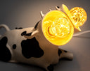 Lamp designed as a cow's body sitting on the ground, with 2 light bulbs coming from 2 separate cow heads conjoined to the same neck.