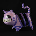 Ceramic sculpture of the Cheshire cat, stylized to have large human like teeth and an empty coil for a body.  It looks off to the side with a slightly mischievous look.