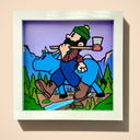 A framed square artwork featuring a cartoon-style lumberjack walking with a giant blue ox through a forest with mountains and a stream. The artwork is presented in a white frame against a light beige wall.