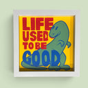 A square framed artwork featuring a green cartoon dinosaur and the text 'LIFE USED TO BE GOOD' in red and blue on a yellow background, mounted on a light green wall.