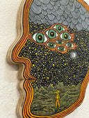 Die cut piece of wood in the shape of a head profile, painted to have 8 eyes and a starry sky background with rows of clouds and a cratered ground surface. A small creature walks on 2 legs on the surface.