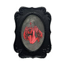 A gothic-style framed artwork featuring a red angel with wings, with her head bowed down sadly and a star shard piercing through her back, enclosed in an ornate black frame.