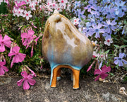 Ceramic sculpture of a brown character with a rounded body, small ears and eyes and skinny legs and no other body features.