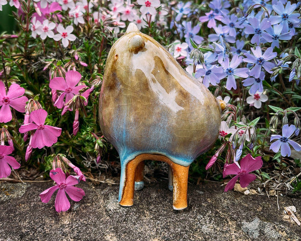 Ceramic sculpture of a brown character with a rounded body, small ears and eyes and skinny legs and no other body features.