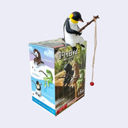 Plastic figurine of a penguin, sitting on a box and holding out a fishing rod with a line hanging from it.