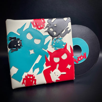 Vinyl fabric sculpture of a music record coming out of a square sleeve. The sleeve is white with different sized Big Boss Robot cut outs, red, blue and black. One holds a small white bunny under its arm.