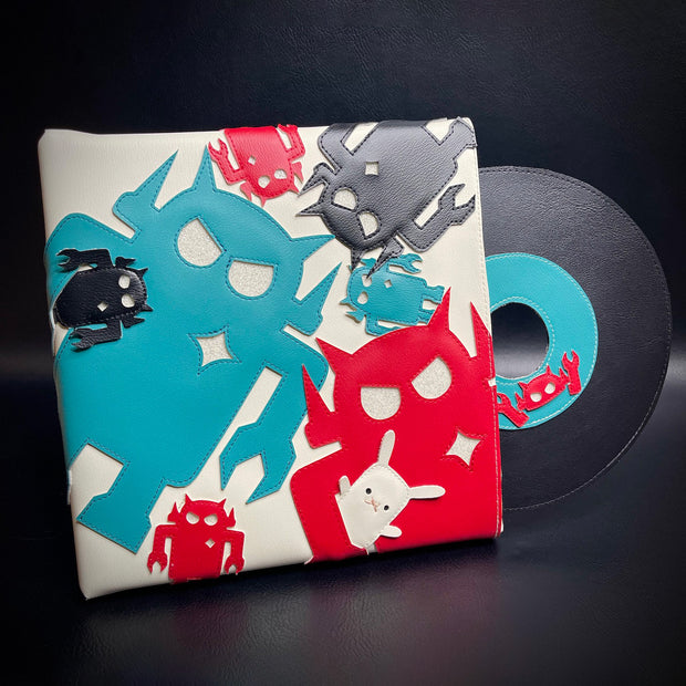 Vinyl fabric sculpture of a music record coming out of a square sleeve. The sleeve is white with different sized Big Boss Robot cut outs, red, blue and black. One holds a small white bunny under its arm.