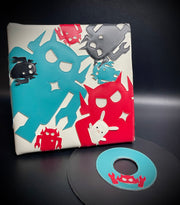 Vinyl fabric sculpture of a music record coming out of a square sleeve. The sleeve is white with different sized Big Boss Robot cut outs, red, blue and black. One holds a small white bunny under its arm.