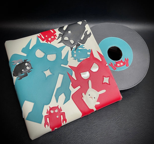 Vinyl fabric sculpture of a music record coming out of a square sleeve. The sleeve is white with different sized Big Boss Robot cut outs, red, blue and black. One holds a small white bunny under its arm.