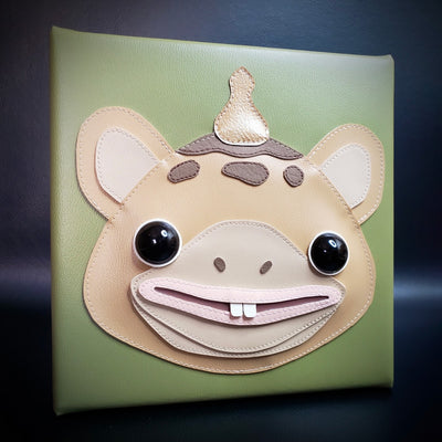Square panel wrapped in vinyl fabric, with a flat sculpture of Booska, a mouse like monster with a antenna coming out of its head. It has large black eyes which raise off the piece slightly.