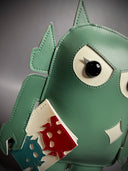 Sage green vinyl fabric plush of a Big Boss Robot, slightly shorter and with large eyes. It holds a small white magazine with a red and a blue robot on it.