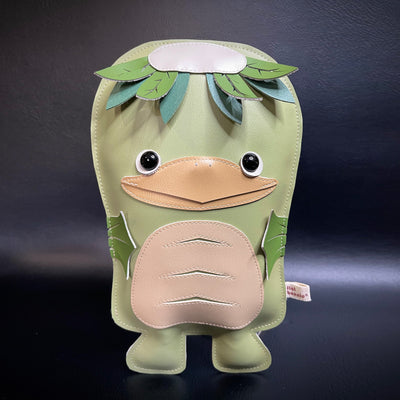 Vinyl plush sculpture of a green kappa, with leaves coming off the top of its head and a beak. It has fins for hands.