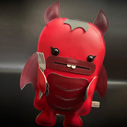 Red vinyl plush of a devil creature with an outlined mouth and buckteeth. It has horns, wings and a fork under one of its arms. 