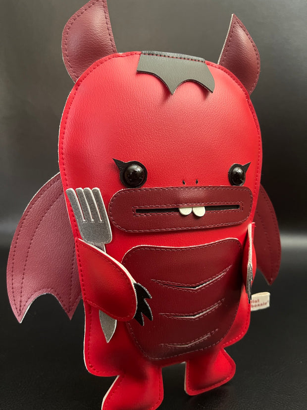 Red vinyl plush of a devil creature with an outlined mouth and buckteeth. It has horns, wings and a fork under one of its arms.