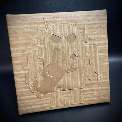 Square canvas covered in wood grain pleather fabric, with a Big Boss Robot holding a small rabbit under its arm in the center of the piece. The robot is the same wood grain pattern, though in a different direction so it is slightly more visible.