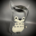 Flat vinyl plush doll of a stylized Totoro with large eyes and a wide smile. It holds a black leaf over its head.