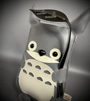 Flat vinyl plush doll of a stylized Totoro with large eyes and a wide smile. It holds a black leaf over its head.