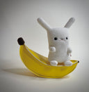 Plush sculpture of a small white bunny sitting on a pleather banana.