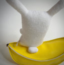 Plush sculpture of a small white bunny sitting on a pleather banana.