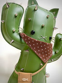 VInyl fabric plush doll of a cactus with a cat face and cat ears. It has metal spikes, a brown fabric bandana and a small pleather pouch.
