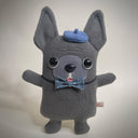 Flat plush doll of a gray French Bull dog with pointy ears, standing on 2 legs like a person. It has black bead eyes and wears a navy bowtie and matching beret cap.