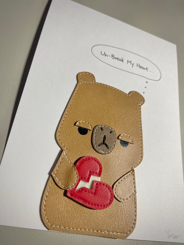 Vinyl flat plush art figure of a capybara with an apathetic expression, holding a broken red heart in its hands. It has a thought bubble that says "un-break my heart..."