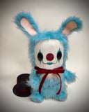 A blue furry bunny costume plush toy with a white face, red nose, black eye makeup, and a red bow tie.