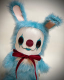 A blue furry bunny costume plush toy with a white face, red nose, black eye makeup, and a red bow tie.