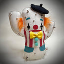 A cactus-shaped vinyl plush dressed like a clown with silver metal spikes, a black beret, orange and black hair accents, a red and white striped vest, a yellow bow tie, and turquoise details, shown on a neutral gray background.