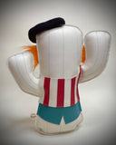 A cactus-shaped vinyl plush dressed like a clown with silver metal spikes, a black beret, orange and black hair accents, a red and white striped vest, a yellow bow tie, and turquoise details, shown on a neutral gray background.