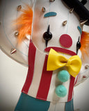 A cactus-shaped vinyl plush dressed like a clown with silver metal spikes, a black beret, orange and black hair accents, a red and white striped vest, a yellow bow tie, and turquoise details, shown on a neutral gray background.