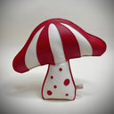 A mushroom-shaped plush made of textured faux leather, featuring alternating red and white stripes on the cap and a white base with red polka dots, set against a neutral gray background.