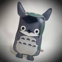 Flat vinyl fabric plush sculpture of Totoro, smiling with a leaf umbrella overhead.