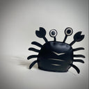 VInyl plush of a black crab with cute, google-y eyes that are also made out of vinyl.