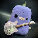 Flat plush sculpture of an ube, a purple root vegetable. Plush has different sized eyes and a bucktooth mouth. It holds a light purple electric guitar.