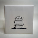A vinyl fabric artwork depicting a cartoon rabbit laying flat on its back atop a dog house, crafted from off-white leather with black stitched outlines and details, displayed on a textured off-white background.