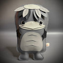 Grayscale vinyl plush doll with a flat body shape of a Kappa, with a large bird-like beak and a turtle like face, with a flat top head and leaves around it.