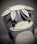 Grayscale vinyl plush doll with a flat body shape of a Kappa, with a large bird-like beak and a turtle like face, with a flat top head and leaves around it.