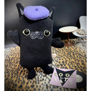 Black plush sculpture of a flat cat, with a purple beret and a vinyl sleeved record at its feet that reads "Cool for Cats." Its arms are posed in a welcoming, excited way.